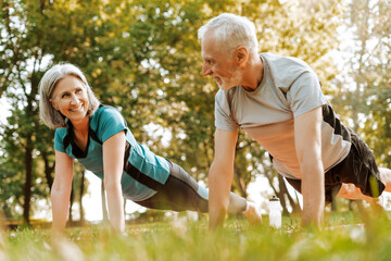 Fototapeta premium Senior couple doing plank exercise together outdoors in park, outdoors