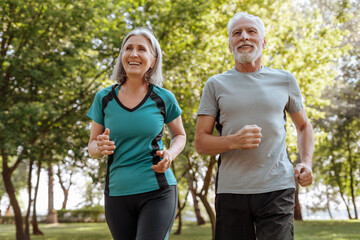 Obraz premium Smiling senior couple running in park wearing sportswear outdoors, sport, active lifestyle concept