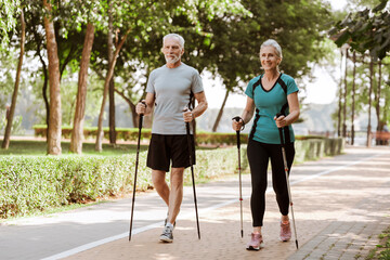 Happy, smiling senior couple training together nordic walking in park, outdoors