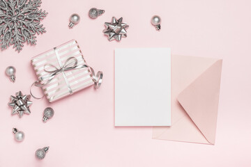 Christmas greeting card, background. Pink gift box with silver ribbons and Christmas tree balls and pink envelope with blank card on pink background. Pink Christmas.