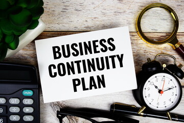Business Continuity plan text with calculator, magnifying glass and alarm clock on wooden background