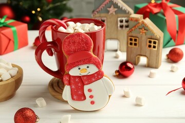 Delicious cookie in shape of snowman, cup with cocoa and Christmas decor on white wooden table