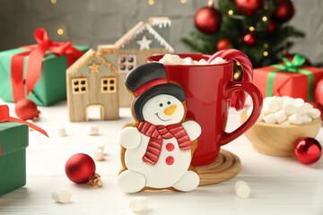 Delicious cookie in shape of snowman, cup with cocoa and Christmas decor on white wooden table