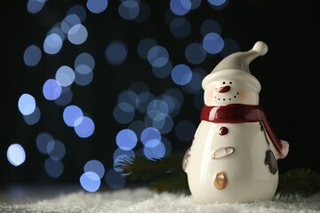 Cute decorative snowman on artificial snow against blurred lights. Space for text
