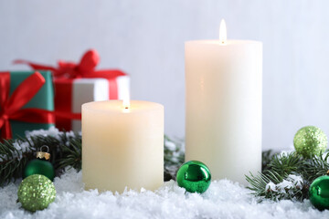 Burning candles, baubles and fir branches on artificial snow, closeup. Christmas atmosphere