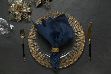 Christmas place setting with plate, cutlery, glass and festive decor on black table, flat lay
