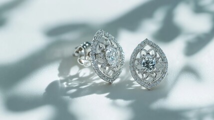 A pair of diamond earrings with intricate designs, resting on a white background. The clarity of the diamonds and the shine of the metal are perfectly captured in the clean setting.