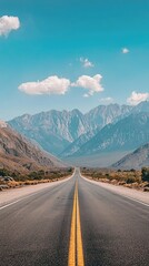 Fototapeta premium A solitary highway stretches towards the horizon, framed by towering mountains and a clear blue sky. The yellow lines guide the way, promising adventure and unknown destinations.