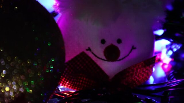 Una toma de cerca de una cara de un mu&ntilde;eco de nieve rodeado de bolas de navidad y luces de colores. Decoraci&oacute;n de navidad y fin de a&ntilde;o