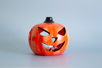 Ceramic Halloween pumpkin with lit candle flame against a silver grey background