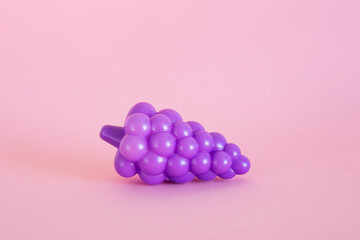 Plastic purple grapes against a pink backdrop 