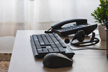 An office telephone nest to black computer keyboard and mouse are on a desk