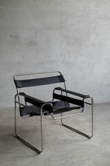 Modern black leather chair with a chrome frame in a minimalist interior against a concrete wall...