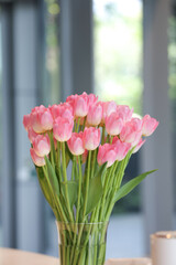 Pink tulips in a glass vase are placed on the table. Tulips in a vase with blurred background. 