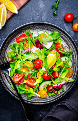 Vegan vegetable salad with tomatoes, cucumber, red onion, lettuce and arugula. Black background, top view