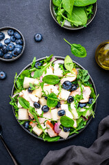 Fresh salad with sweet melon, grilled chicken breast, onion,  feta cheese, blueberries and mixed herbs, black table background, top view