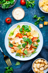 Caesar salad with shrimp, tomatoes, iceberg lettuce, croutons, parmesan cheese and classic dressing. Blue background, top view