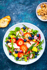 Foodie food salad with strawberry, chicken, arugula, blueberries, avocado and walnuts, blue table., top view