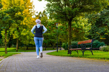 Woman in casual wear and sunglasses walking in city park in early autumn. Back view