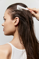 Hair care, styling, personal grooming, beauty, hygiene A profile view of a woman with long, wet hair being combed, set against a soft white background, capturing a moment of self care and beauty