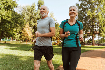 Obraz premium Attractive, smiling senior couple jogging in park maintaining healthy lifestyle