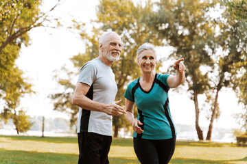 Happy senior couple wearing sportswear pointing and smiling during morning walking routine in park