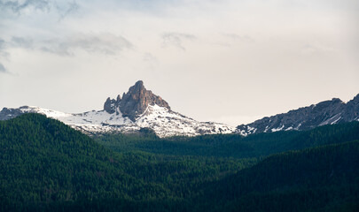 A panoramic view of the Dolomites, with towering mountains and clouds in the background. In the...