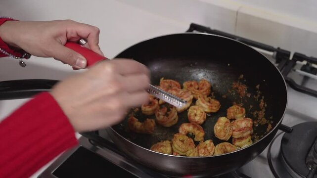 Cooking seafood. Closeup view of a woman hands grating nutmeg over shrimps in the hot wok pan. 