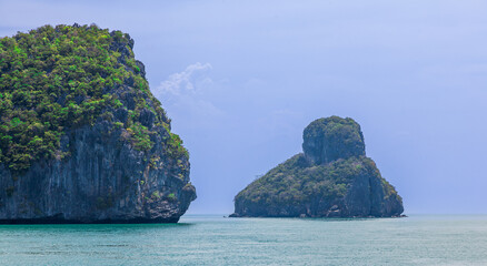 Naklejka premium Two rocky uninhabited islands of Mu Ko Ang Thong National Park, Thailand, during the rainy season, sky and clouds forecasts coming rain. Rock texture, lush foliage and turquoise, calm water.
