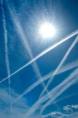 These bright jet contrails or vapor trails criss cross this bright blue sky, backlit by the sun. This illustrates the business travel or aviation transportation and how busy air travel has become.