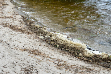 River bank with waves and white foam. White soft foam swaying. Blue water edge on sandy beach. Swirl natural pattern in shallow water. Tranquil scene of beach.