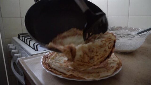 Making pancakes at home. Closeup view fo a male hand removing a fresh crepe heated in a pan, with a spatula, in the kitchen
