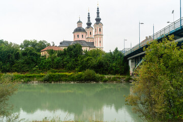 Heiligenkreuzkirche Katholische Kirche in Rosa hinter dem Fluss Drau neben einer Brücke um Sommer an einem bewölkten Tag in Villach in Kärnten Österreich