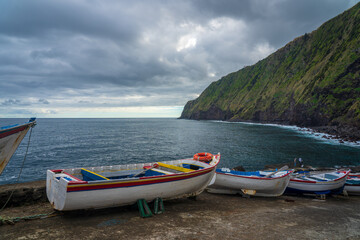 Few boats parked  in front of Atlantic Ocean and tall green cliffs near Nordeste village on Sao Miguel island in Azores archipelago