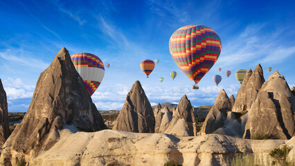 Hot air balloons over unique rock formations of Cappadocia, Turkey. Vibrant balloons contrast with...