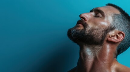 Obraz premium A close-up shot of a muscular individual tilting their head back against a calming blue backdrop, capturing intensity, strength, and the beauty of physical form.