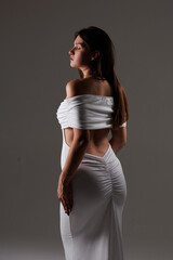 
Beautiful young pregnant brunette girl. A woman waiting for a baby in a white dress with bare shoulders in the studio. Artistic smudges in the photo