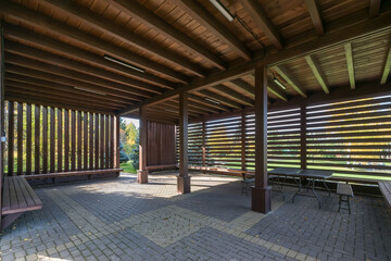 A spacious wooden gazebo, illuminated by the rays of the sun, in the park on an autumn day.