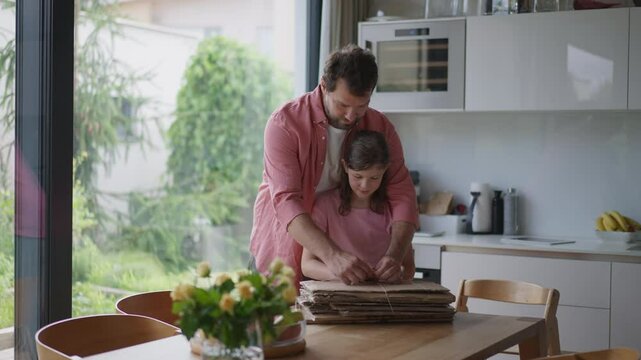 Father and girl preparing cardboard boxes for recycling, working in kitchen together. Sustainable living.