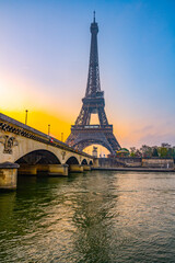 Fototapeta premium As dawn breaks, the Eiffel Tower stands majestically over the Seine River, casting reflections on the water while the city awakens in soft morning light.