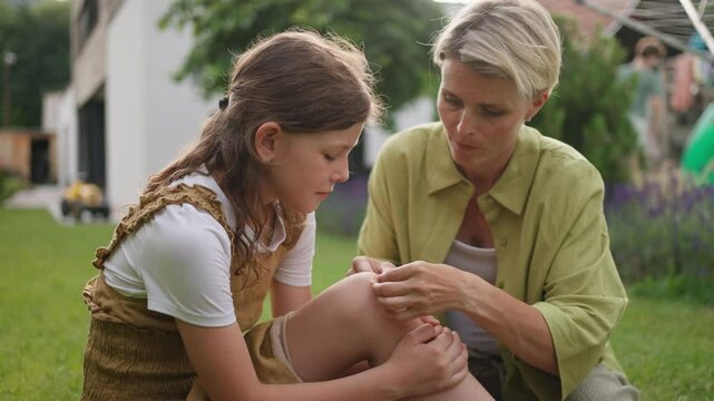 Mother treating her daughter's injury. Injured, bleeding knee after fall. Mom holding band aid and soothing crying girl.
