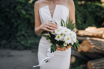Young beautiful bride holding bouquet with white chrysanthemums outdoors. Wedding photography,...