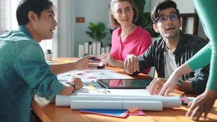 Professional civil engineer handed document while looking at blueprints. Skilled architect team brainstorming idea and planning building design while sitting at meeting table with plans. Symposium.