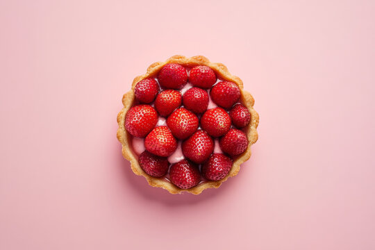 A top view of a strawberry tartlet, with a buttery crust and a perfectly arranged layer of strawberries. The tartlet is displayed on a pale pink background, giving the scene a soft, romantic feel.
