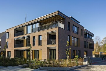 Modern residential building with a brick facade, balconies, and large windows, enjoying the sunlight on a clear day
