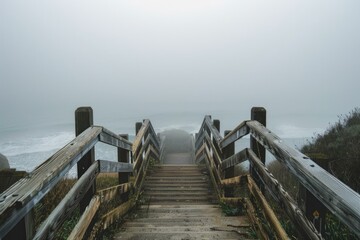 Fototapeta premium Old wooden staircase is leading to a foggy and mysterious beach on a gray overcast day