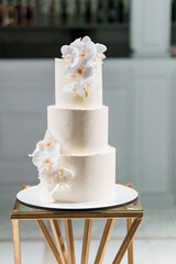 Elegant Three-Tier Wedding Cake Adorned with Delicate White Orchids and Gold Monogram on Modern Geometric Stand