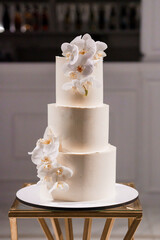Elegant Three-Tier Wedding Cake Adorned with Luxurious White Orchids and Gold Initials on Modern Display Stand