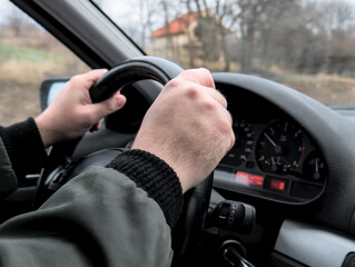 Close-up shot of man's hands firmly holding the steering wheel while driving a car. The man is wearing a dark gray jacket. Winter time