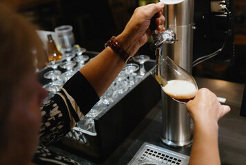 An elderly woman pours draft beer into a glass.